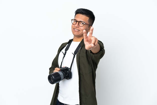 Young Ecuadorian photographer isolated on white wall smiling and showing victory sign