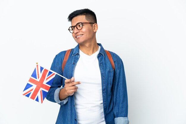 横を見て笑っている白い背景で隔離のイギリス国旗を保持している若いエクアドルの女性
