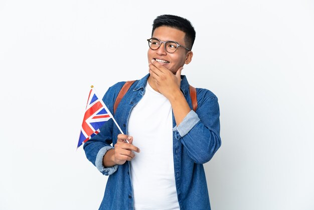 Young Ecuadorian woman holding an United Kingdom flag isolated on white background looking up while smiling