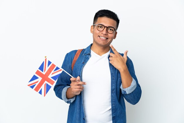 Young Ecuadorian woman holding an United Kingdom flag isolated on white wall giving a thumbs up gesture