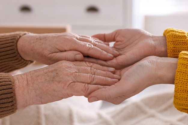 Young and elderly women holding hands together indoors closeup