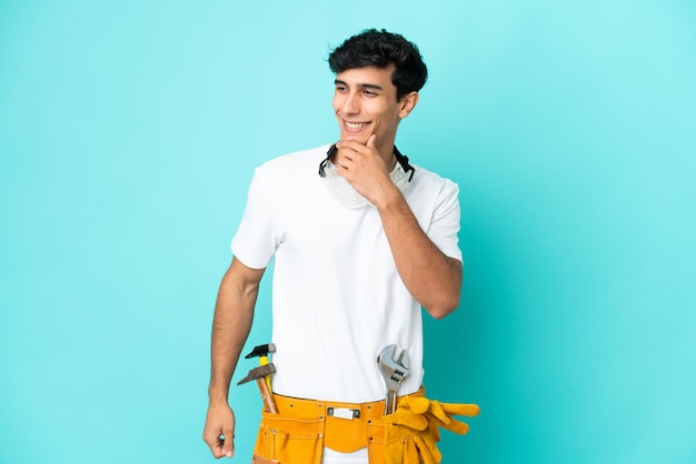 Young electrician Argentinian man isolated on blue background looking to the side and smiling