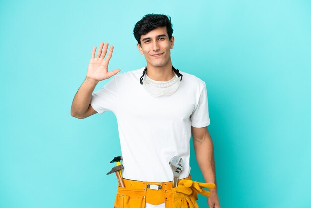 Young electrician Argentinian man isolated on blue background saluting with hand with happy expression