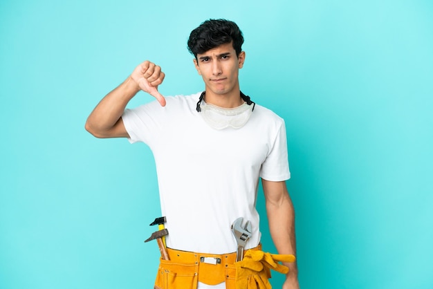 Young electrician Argentinian man isolated on blue background showing thumb down with negative expression