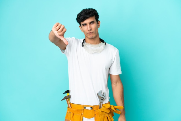 Young electrician Argentinian man isolated on blue background showing thumb down with negative expression