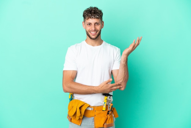 Young electrician blonde man isolated on green background extending hands to the side for inviting to come