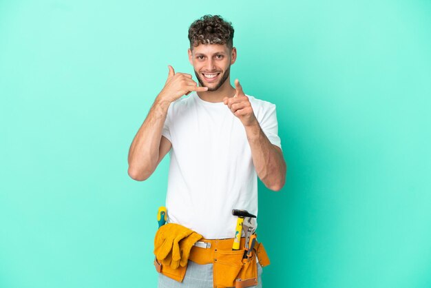 Young electrician blonde man isolated on green background making phone gesture and pointing front