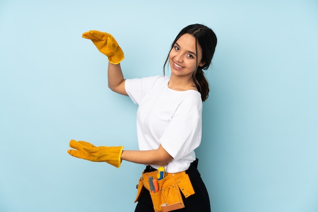 Young electrician woman on blue holding copyspace to insert an ad