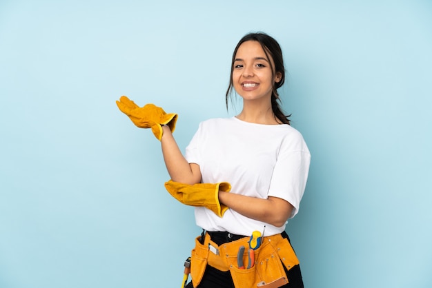 Young electrician woman on blue wall extending hands to the side