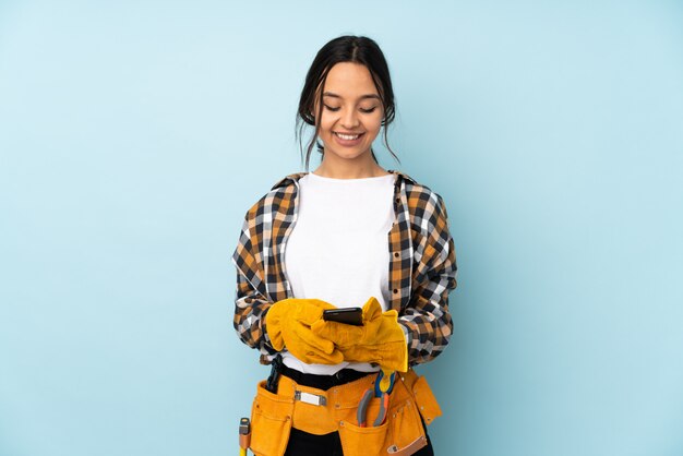 Young electrician woman isolated on blue sending a message with the mobile