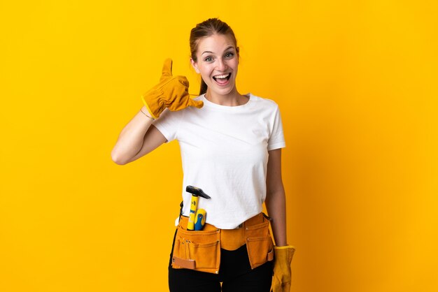 Giovane donna elettricista isolata su sfondo giallo che fa il gesto del telefono. richiamami segno