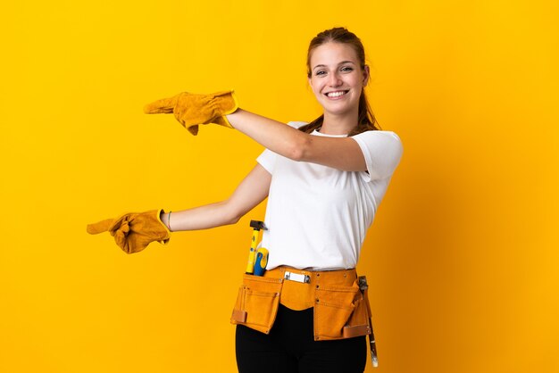 Young electrician woman isolated on yellow pointing finger to the side and presenting a product