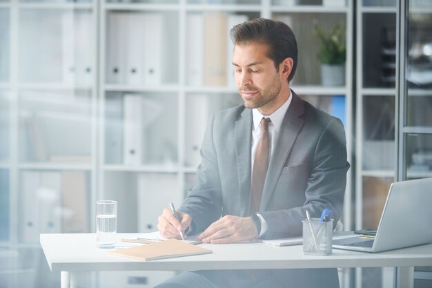 메모를 만드는 동안 새 프로젝트 또는 보고서 작업에 집중하는 젊은 우아한 사업가