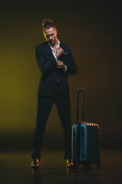 Young elegant caucasian man in tuxedo standing near suitcase