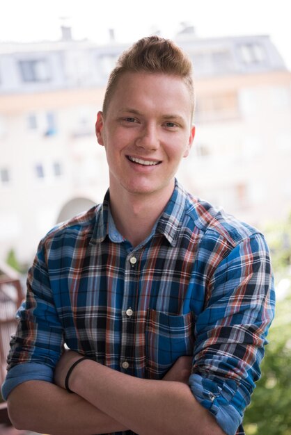 young elegant fashion man standing at balcony with arms crossed and smiling