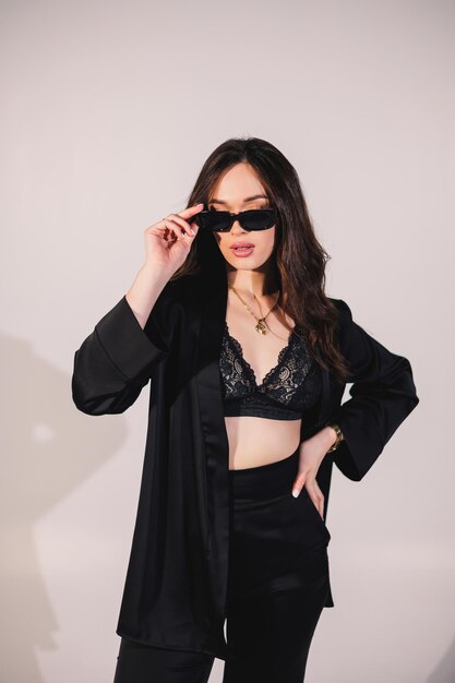 Young elegant stylish woman in a black suit Studio shot A woman in a black suit and black glasses on a white background