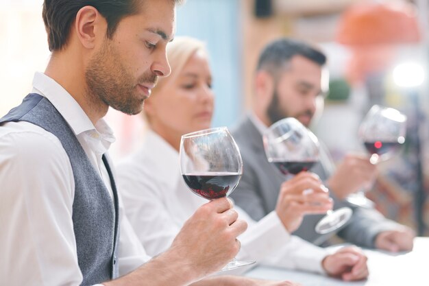 Giovane esperto di cantina o enologo elegante che guarda il vino rosso in bicchiere valutandone il colore e l'odore