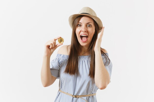 Young elegant woman in blue dress, hat with long hair holding bitcoin coin of golden color isolated on white background. Finance, business online virtual currency concept. Advertising area. Copy space