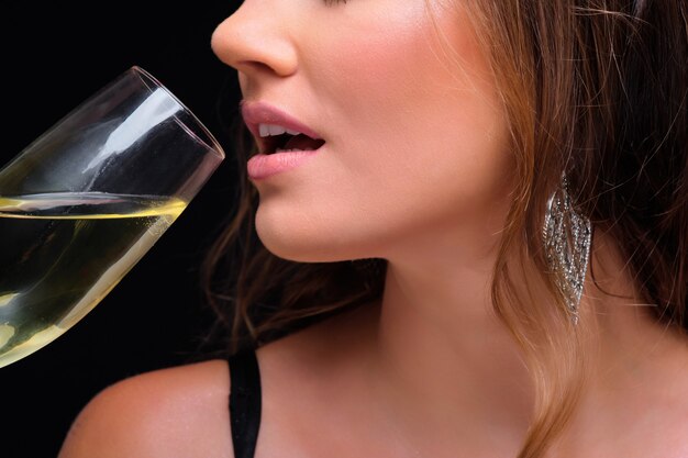 Di giovane donna elegante che beve champagne contro il nero