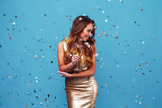 Young elegant woman in golden glitter dress evening makeup holding glass of champagne and celebratin...