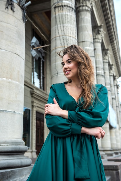 Young elegant woman relaxing and posing for camera near columns in green dress in perfect summer day