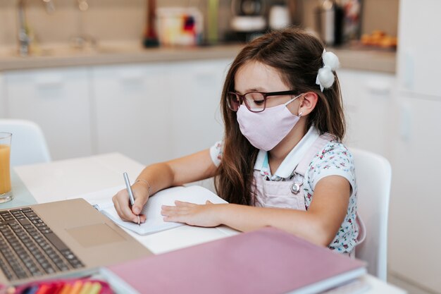 Young elementary school girl with face protective mask watching online education class. Coronavirus or Covid-19 lockdown education concept.