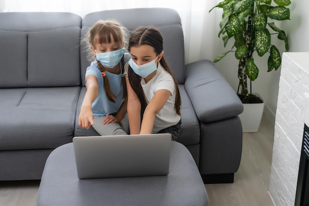 Young elementary school girls with face protective mask watching online education class. Coronavirus or Covid-19 lockdown education concept.