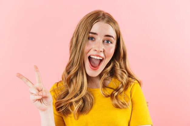 a young emotional cheery optimistic cute girl isolated over pink wall  showing peace gesture.