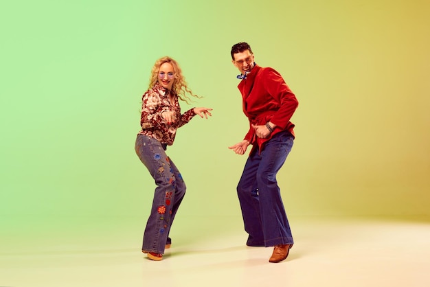 Фото Молодая эмоциональная пара мужчина и женщина в стильной ретро-одежде танцуют против градиента зеленый желтый