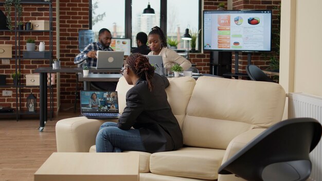 Young employee attending business meeting on videocall, using laptop with internet connection. Woman talking to colleagues on online videoconference, remote communication on teleconference call.