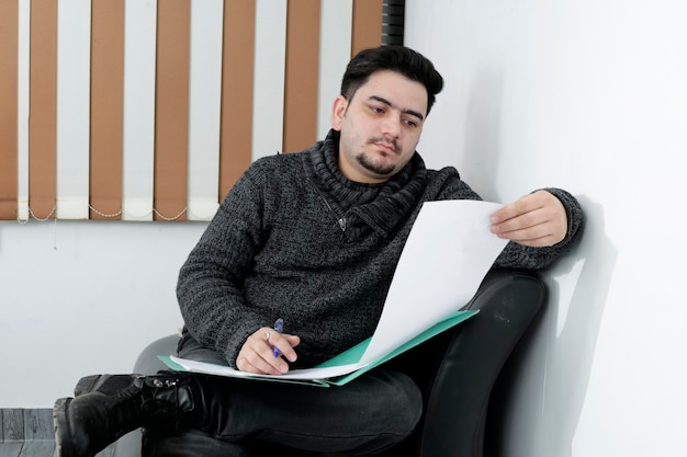 A young employee is sitting on couch and holding paper in hand.