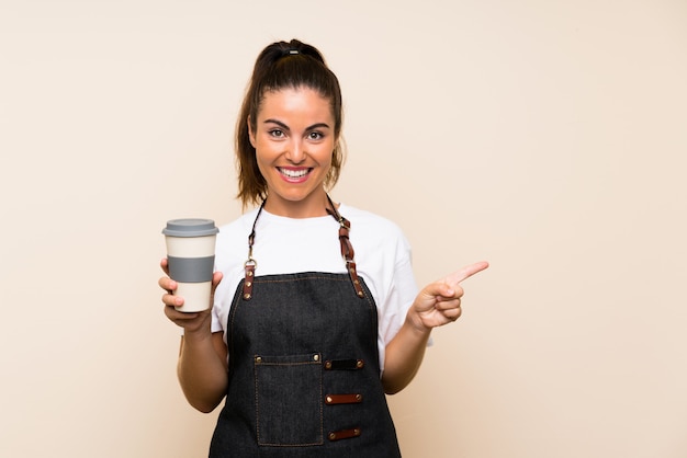 Young employee woman holding a take away coffee surprised and pointing finger to the side