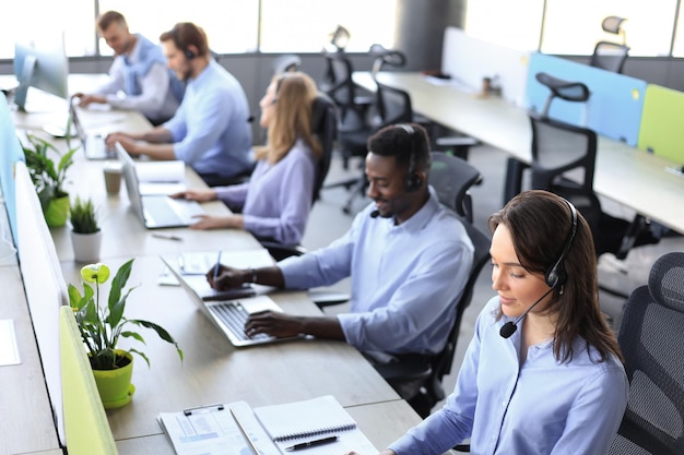 Young employee working with a headset and accompanied by her team