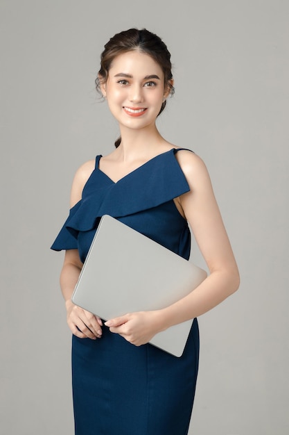 Young energetic Asian business woman holding laptop on gray background