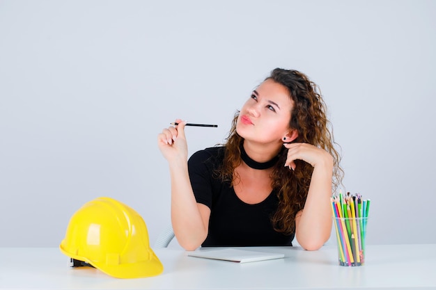 Young engineer girl is looking up by holding pencil on white background