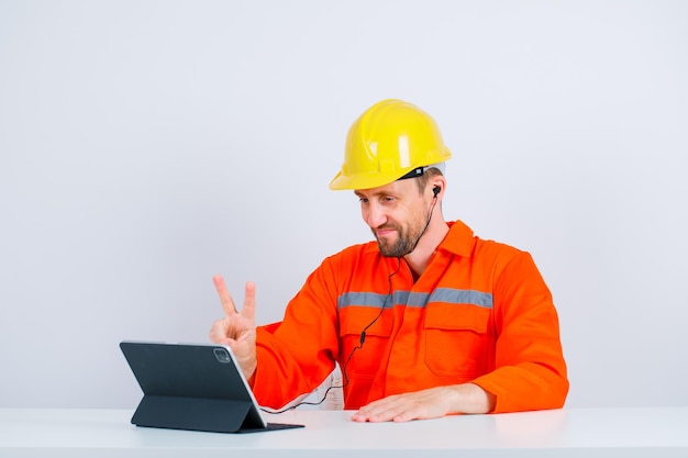 Young engineer is showing two gesture by sitting in front of his tablet on white background