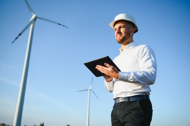 Young engineer man looking and checking wind turbines at field