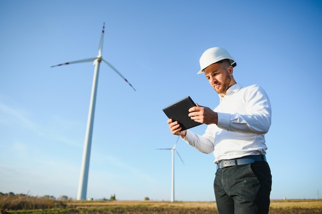 Young engineer man looking and checking wind turbines at field