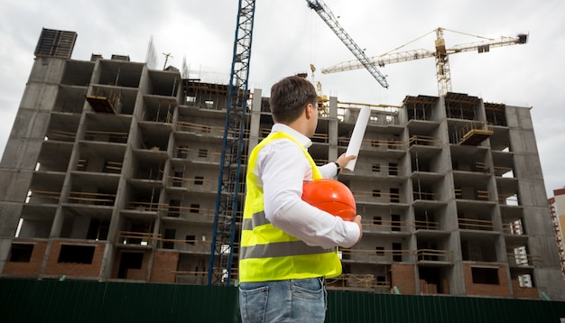 Young engineer pointing at building with rolled blueprints