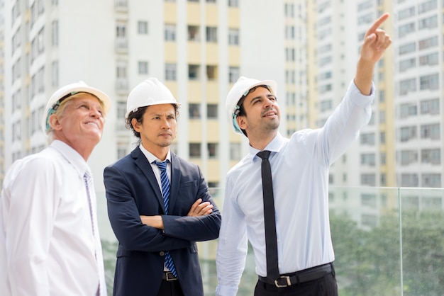 Young engineer pointing at something up to his colleague and serious man in suit 