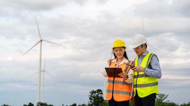 Young engineer team working with report in clipboard against wind turbine farm