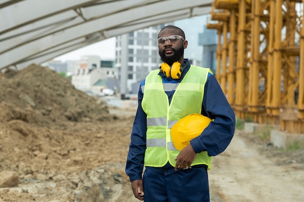 Young engineer in uniform holding protective helmet