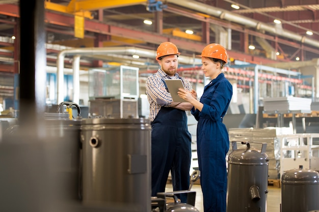 Young engineers in overalls and helmets surfing in the net to get some further information about industrial equipment