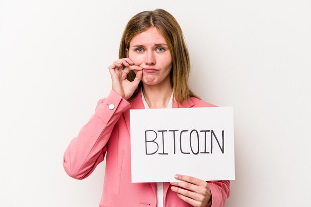 Young English business woman holding a bitcoin placard isolated on white background with fingers on lips keeping a secret