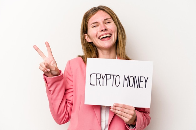 Молодая английская деловая женщина, держащая плакат с криптовалютой на белом фоне, радостно и беззаботно показывает пальцами символ мира.
