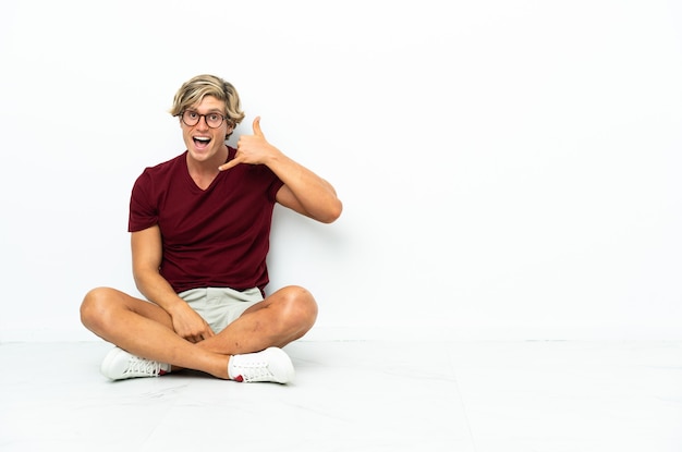 Young English man sitting on the floor making phone gesture. Call me back sign