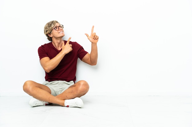 Young english man sitting on the floor pointing with the index finger a great idea