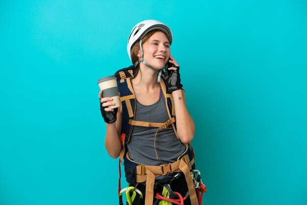 Young English rock climber woman isolated on blue background holding coffee to take away and a mobile