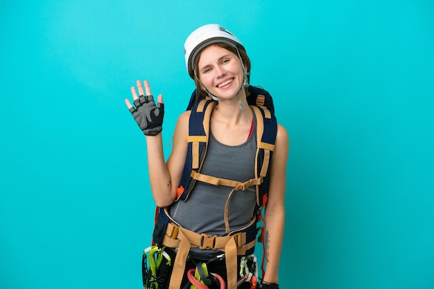Young English rock climber woman isolated on blue background saluting with hand with happy expression