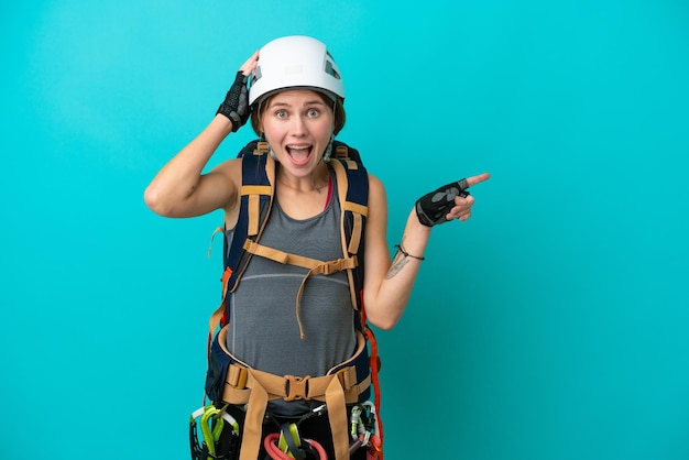 Young English rock climber woman isolated on blue background surprised and pointing finger to the side